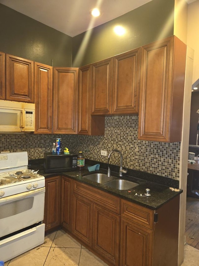 kitchen with white appliances, a sink, dark stone countertops, and tasteful backsplash