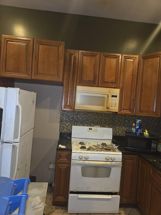 kitchen featuring brown cabinets, dark countertops, decorative backsplash, and white appliances