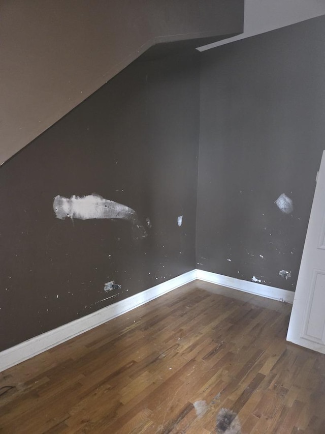 empty room featuring lofted ceiling, baseboards, and wood finished floors