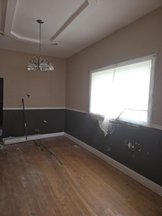 unfurnished room with a raised ceiling, hardwood / wood-style floors, baseboards, and an inviting chandelier