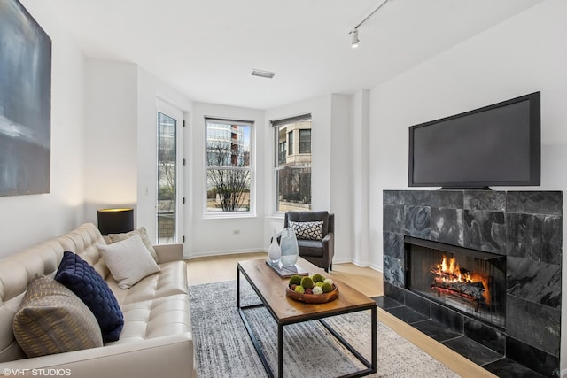 living room with baseboards, track lighting, a fireplace, visible vents, and wood finished floors