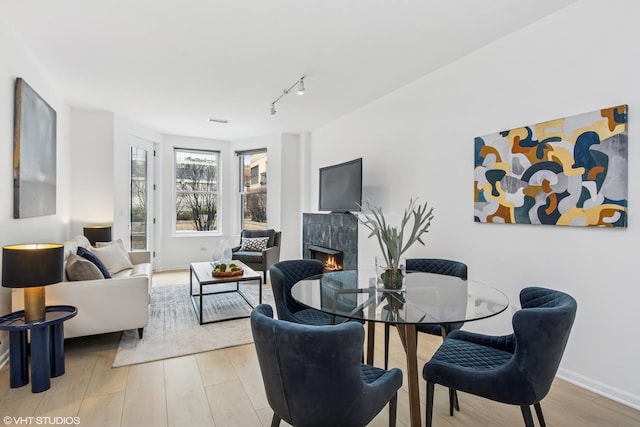 dining room with a high end fireplace, track lighting, baseboards, and wood finished floors
