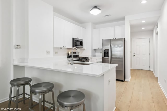 kitchen featuring a peninsula, visible vents, a breakfast bar area, appliances with stainless steel finishes, and light wood finished floors