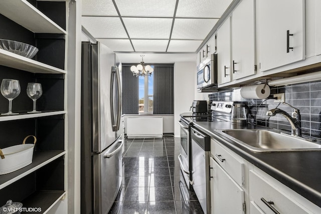 kitchen featuring stainless steel appliances, a sink, white cabinetry, a chandelier, and backsplash