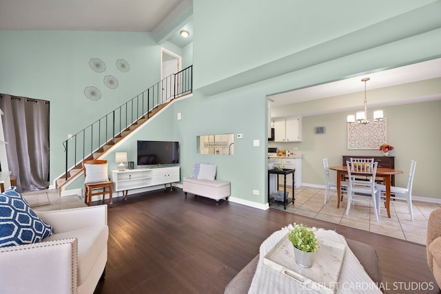 living area with an inviting chandelier, wood finished floors, stairs, baseboards, and high vaulted ceiling