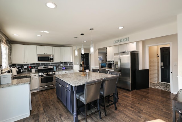kitchen featuring white cabinets, light stone counters, a sink, a center island, and stainless steel appliances