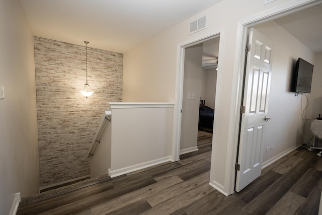 hall featuring visible vents, dark wood finished floors, baseboards, and an upstairs landing