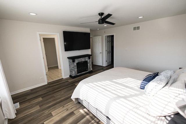 bedroom with a stone fireplace, visible vents, wood finished floors, baseboards, and recessed lighting