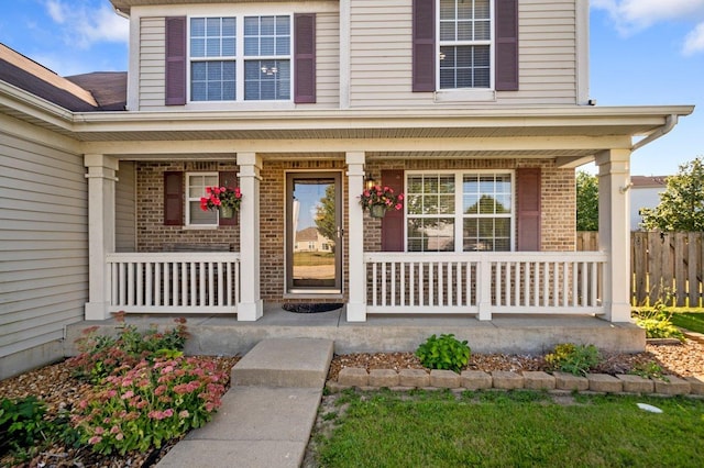 doorway to property featuring a porch, fence, and brick siding