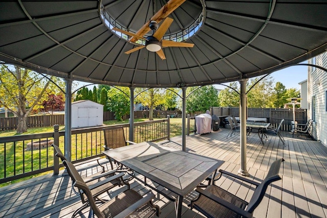 wooden deck with a fenced backyard, outdoor dining space, a gazebo, and a shed