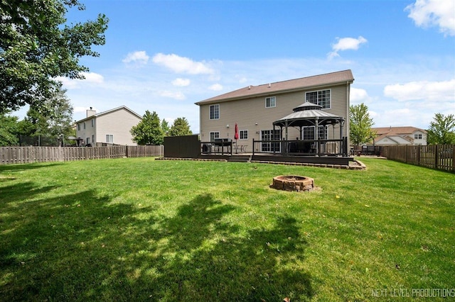 rear view of house with a wooden deck, a gazebo, a fenced backyard, an outdoor fire pit, and a yard