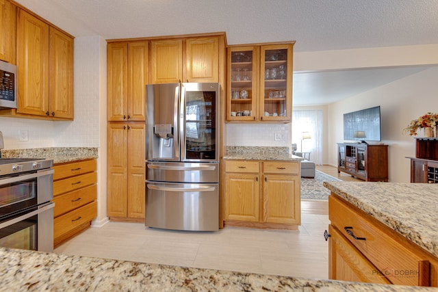 kitchen with light stone counters, decorative backsplash, and stainless steel appliances