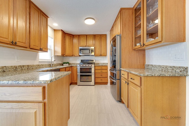 kitchen with stainless steel appliances, light stone countertops, a sink, and decorative backsplash