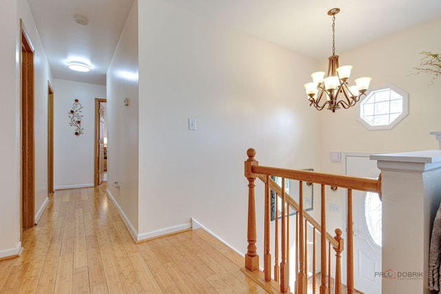 corridor with a chandelier, light wood-style floors, baseboards, and an upstairs landing