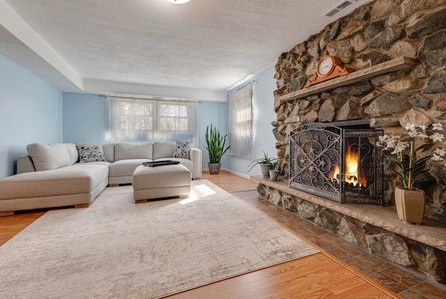 living area featuring a textured ceiling, wood finished floors, a fireplace, and visible vents