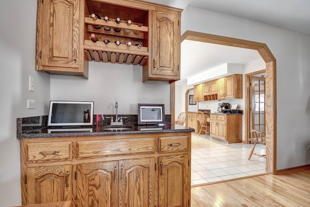 kitchen featuring open shelves, light wood-type flooring, dark stone counters, arched walkways, and a sink