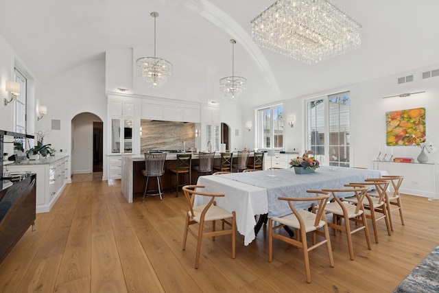 dining area with high vaulted ceiling, arched walkways, an inviting chandelier, and light wood-style flooring