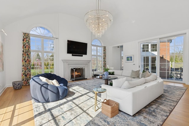living room with wood-type flooring, baseboards, high vaulted ceiling, a notable chandelier, and a lit fireplace