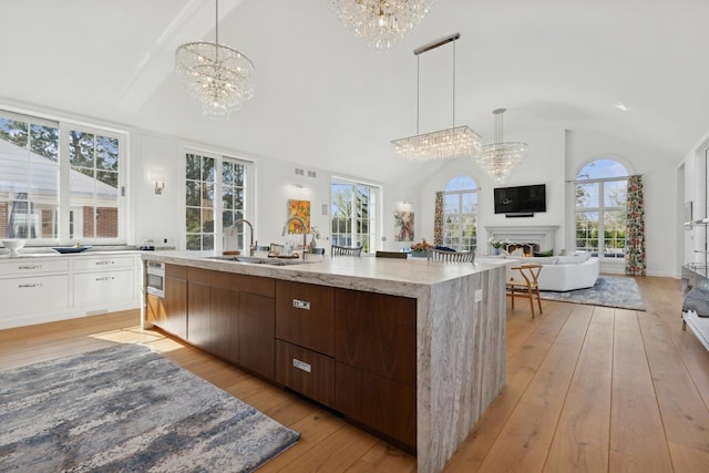 kitchen featuring an inviting chandelier, a large island with sink, light wood-style floors, and a sink
