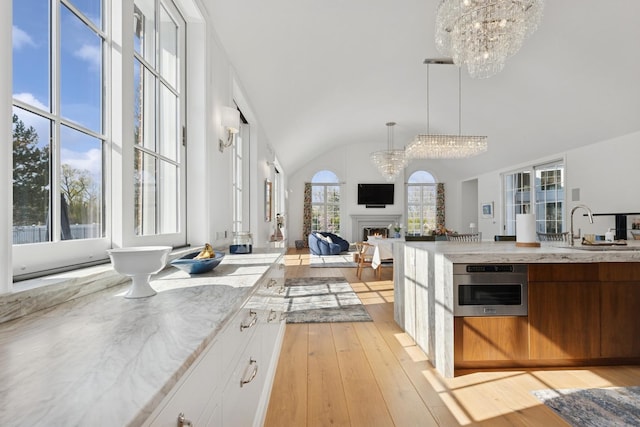 kitchen featuring lofted ceiling, a sink, light wood-style floors, a warm lit fireplace, and an inviting chandelier
