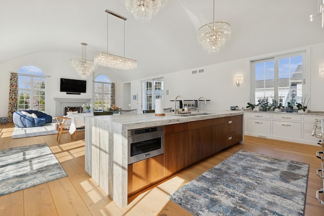 kitchen with a sink, a chandelier, visible vents, light wood-style flooring, and vaulted ceiling