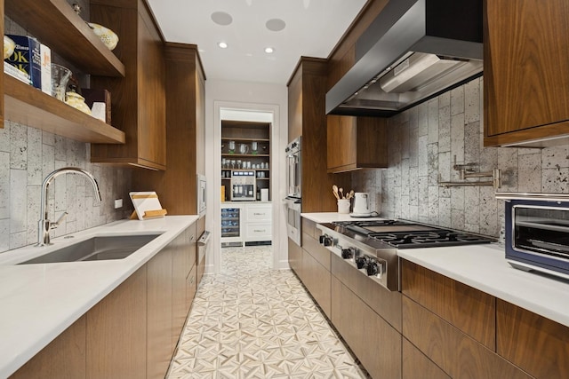 kitchen with a sink, stainless steel appliances, tasteful backsplash, wall chimney range hood, and light countertops