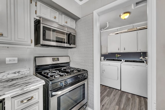 kitchen featuring washing machine and dryer, stainless steel appliances, white cabinetry, and light wood-type flooring