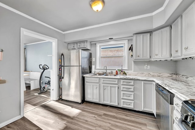 kitchen featuring light wood-style flooring, appliances with stainless steel finishes, ornamental molding, and a sink