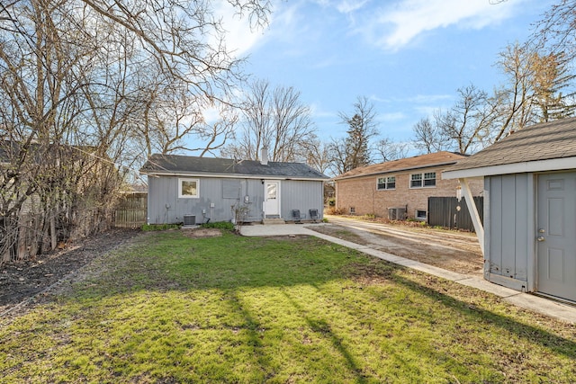 rear view of house with a yard, an outbuilding, central AC, and fence