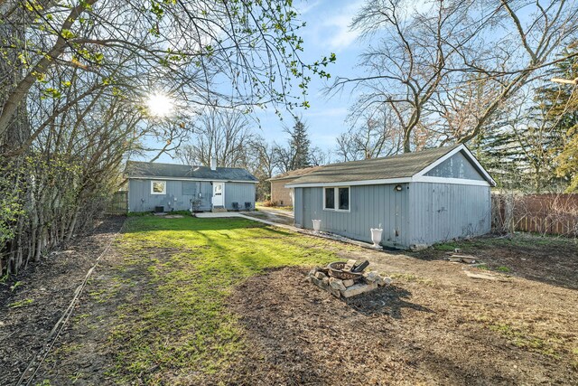 back of house featuring a lawn, an outdoor fire pit, a fenced backyard, an outdoor structure, and roof with shingles