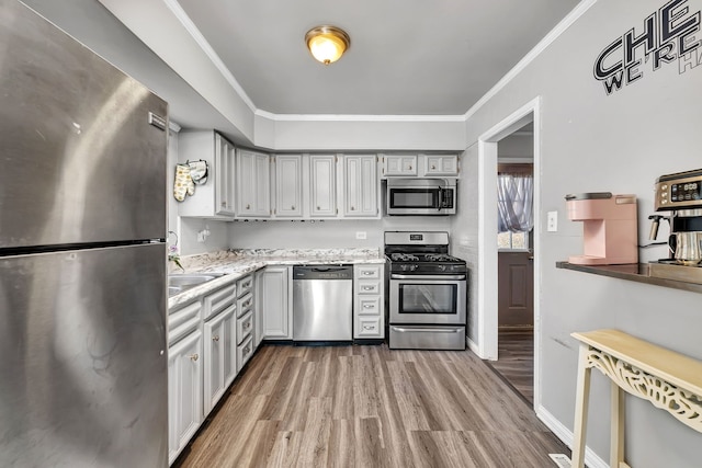 kitchen featuring stainless steel appliances, a sink, baseboards, wood finished floors, and ornamental molding