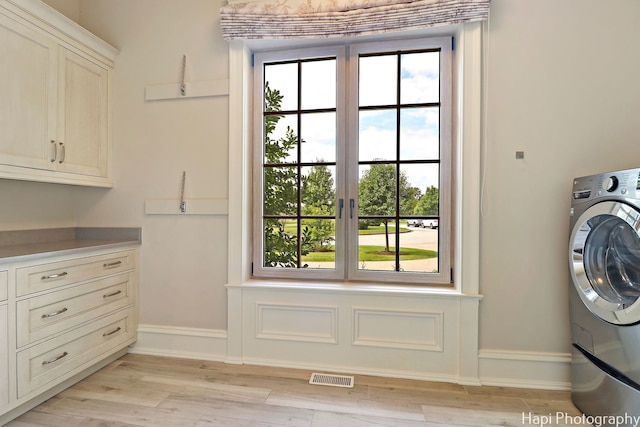 laundry area featuring baseboards, washer / dryer, visible vents, cabinet space, and light wood finished floors