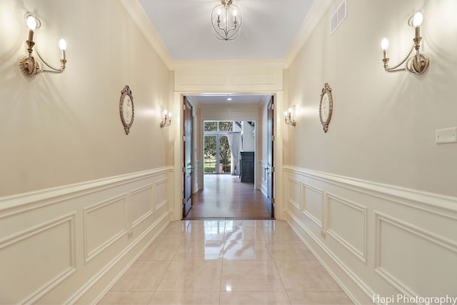 corridor with crown molding, a decorative wall, a notable chandelier, and visible vents