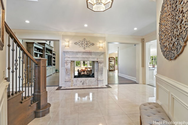 foyer with a decorative wall, light tile patterned floors, a multi sided fireplace, a wainscoted wall, and stairway