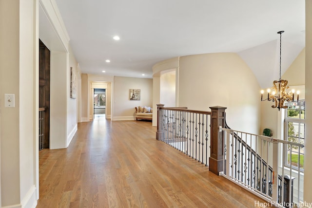 corridor featuring plenty of natural light, an upstairs landing, a notable chandelier, and wood finished floors
