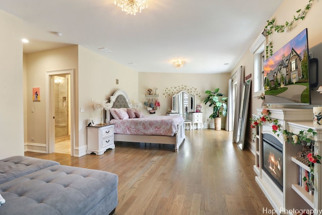 bedroom with baseboards, connected bathroom, a glass covered fireplace, and wood finished floors