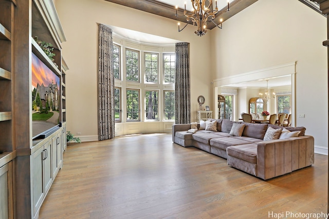 living room with a chandelier, light wood-style floors, a towering ceiling, and baseboards
