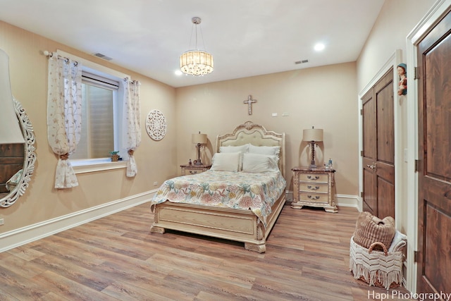 bedroom with visible vents, baseboards, a notable chandelier, and wood finished floors