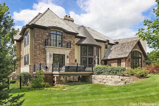 view of front of house with a chimney, brick siding, a front yard, and a balcony