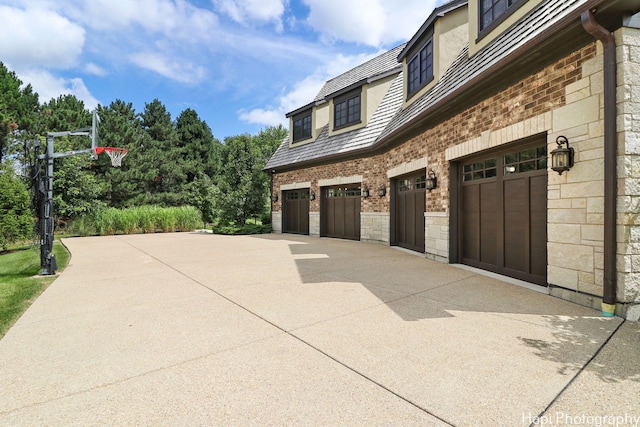 view of side of property featuring brick siding, an attached garage, stone siding, and concrete driveway
