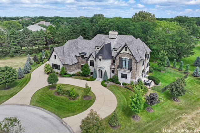 view of front of house featuring curved driveway, a front yard, stone siding, fence, and a chimney