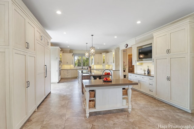 kitchen featuring pendant lighting, ornamental molding, recessed lighting, a kitchen island with sink, and decorative backsplash