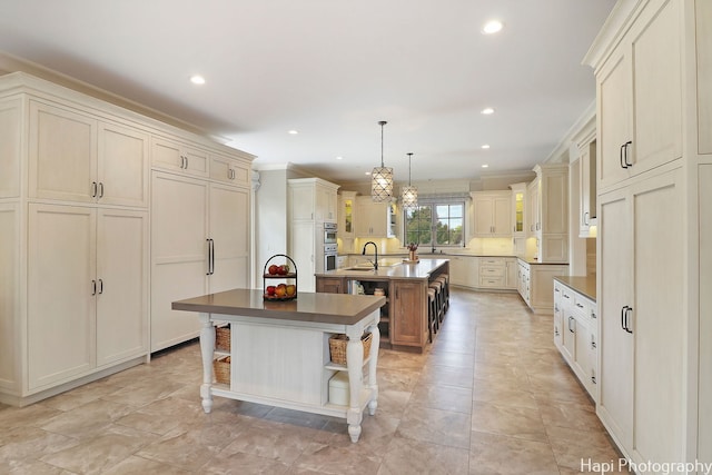 kitchen with recessed lighting, an island with sink, crown molding, double oven, and a sink