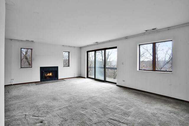 unfurnished living room featuring carpet floors, baseboards, visible vents, and a fireplace with flush hearth
