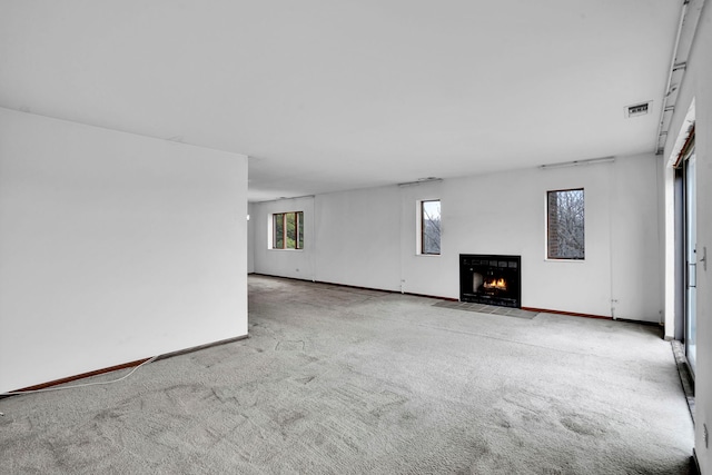 unfurnished living room with a fireplace with flush hearth, baseboards, visible vents, and carpet floors