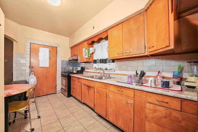 kitchen featuring light tile patterned floors, gas stove, light countertops, a sink, and backsplash