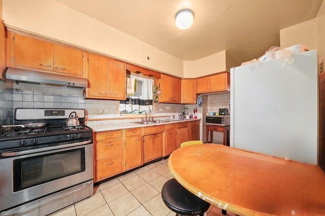 kitchen with light tile patterned floors, a sink, light countertops, under cabinet range hood, and stainless steel appliances
