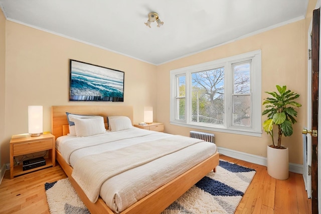 bedroom with ornamental molding, radiator heating unit, light wood-style floors, and baseboards