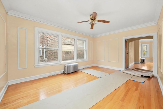 exercise room with radiator, a ceiling fan, ornamental molding, baseboards, and hardwood / wood-style flooring