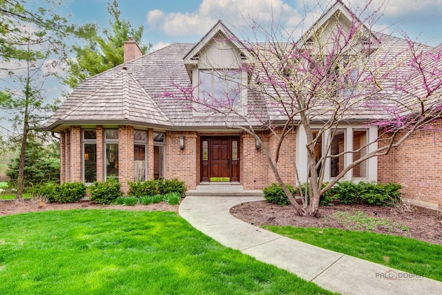 tudor home with brick siding, a chimney, and a front yard